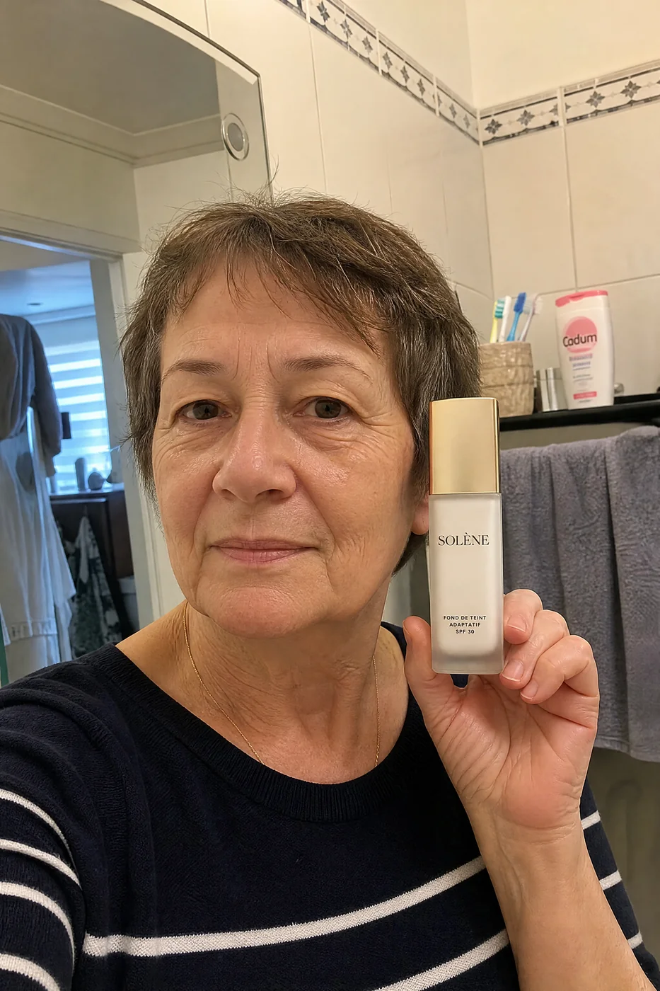 Nicole, 64 ans, tient son flacon de fond de teint Solène dans sa salle de bain