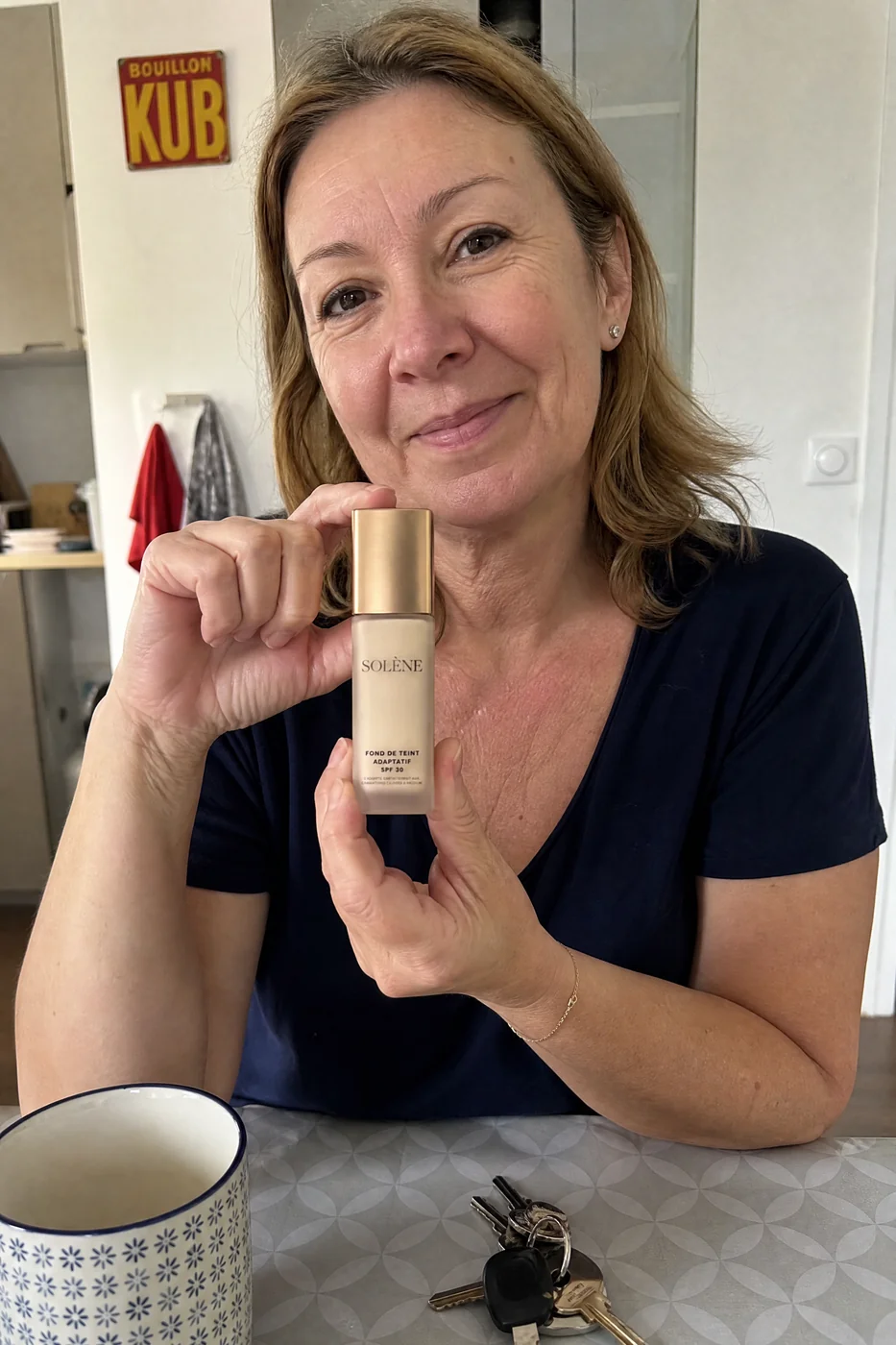Corinne, 56 ans, montre son flacon de fond de teint Solène, à table